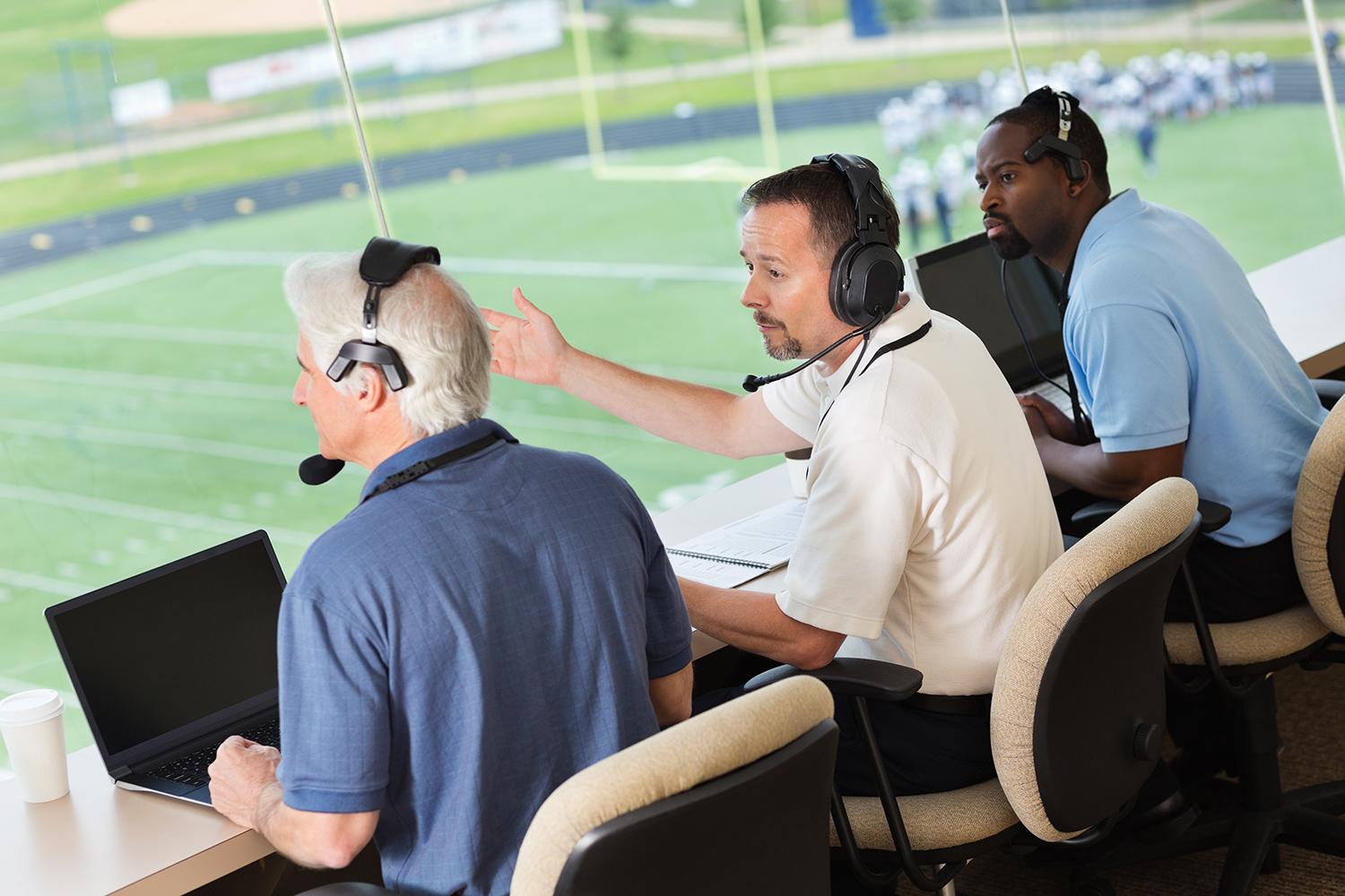 Broadcast crew wearing headsets working at laptops above a sports field